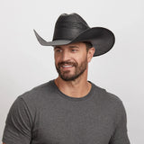Man wearing a black cowboy hat against a plain background